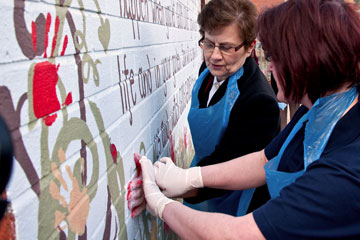 General Linda Bond adds a palm-print to the mural wall next to the Growing Together community gardens