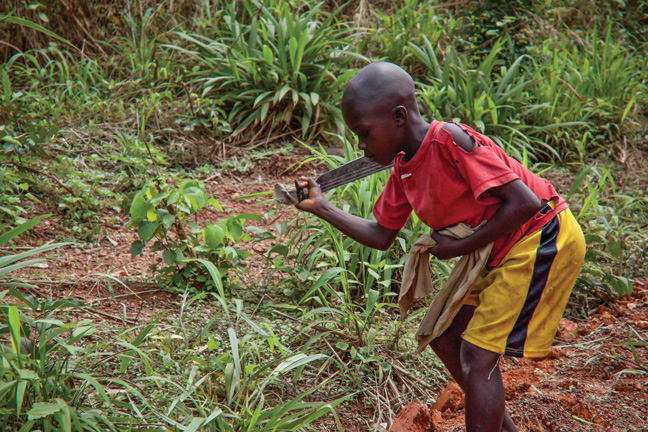 A boy uses a machete to cut weeds in Liberia