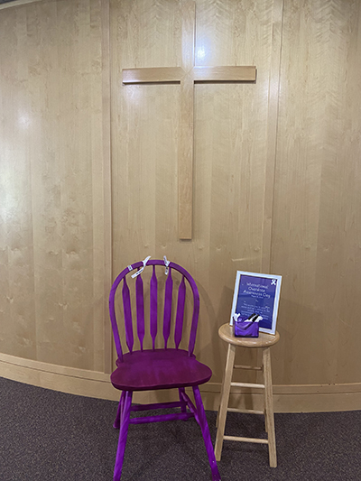 A purple chair, with a small side table and a sign.