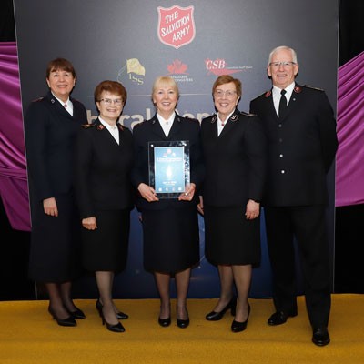 Group of five people standing together, woman in centre holding award
