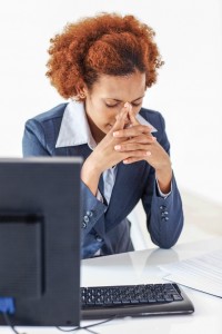 A woman sits at her computer, suffering from pain