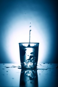 A water drop lands in a full glass of water