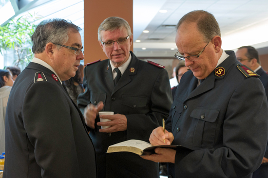 The General signs an Army songbook for Lt-Colonel Doug Hefford, DC, N.L. Div, as Major Ron Millar, DC, Alta. And N.T. Div, looks on