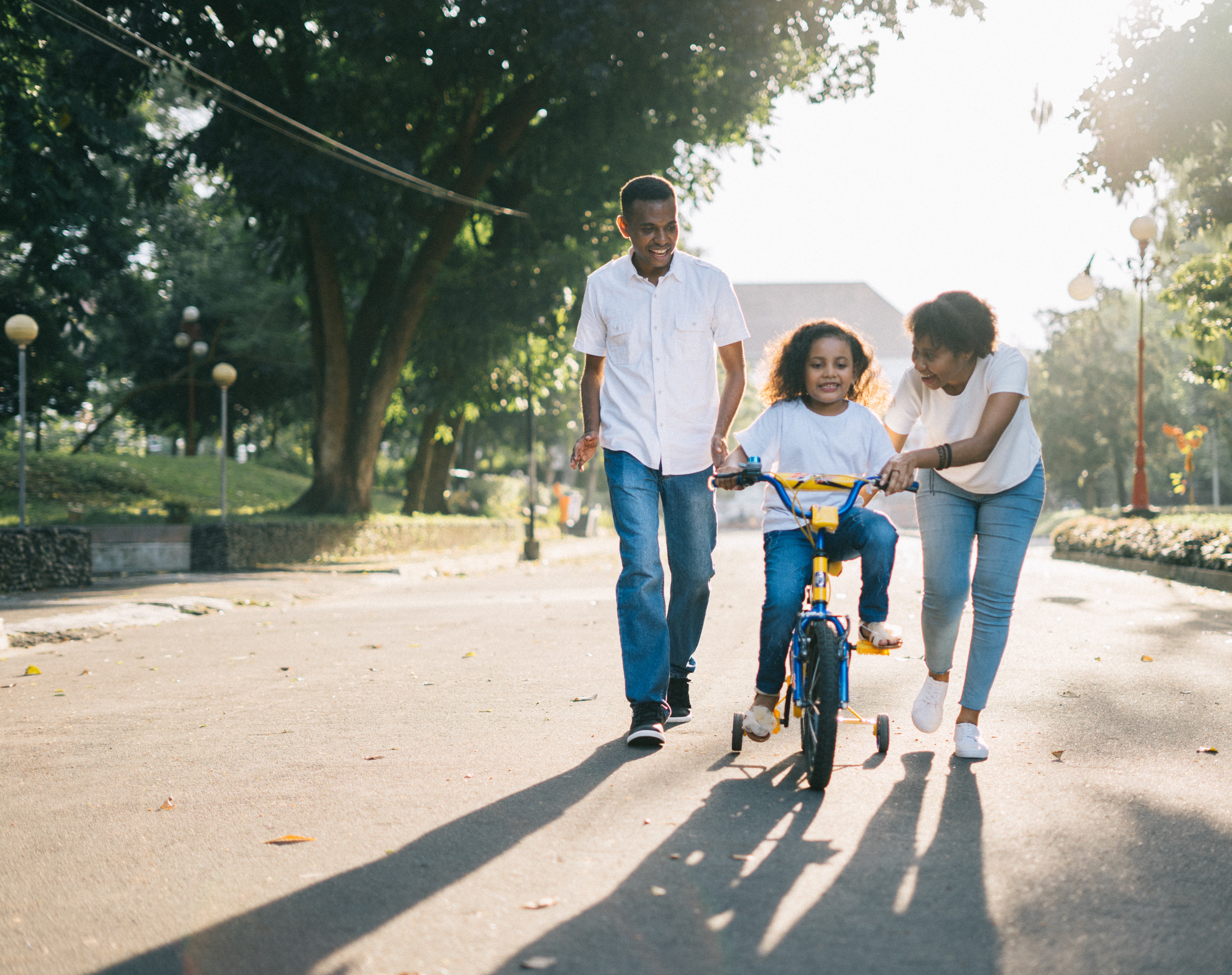 child riding bicycle with mother assisting and father walking alongside