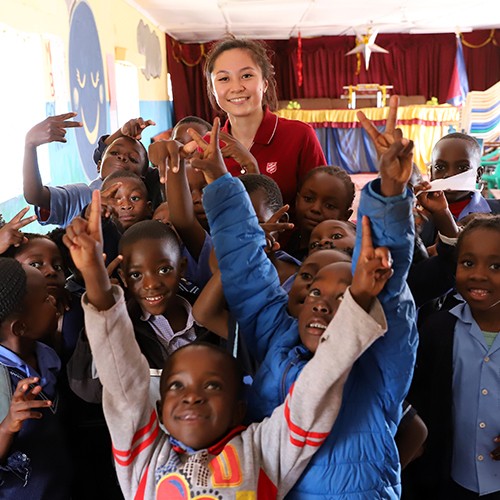 A woman poses joyfully with a group of children, capturing a moment of happiness and togetherness in a vibrant environment.