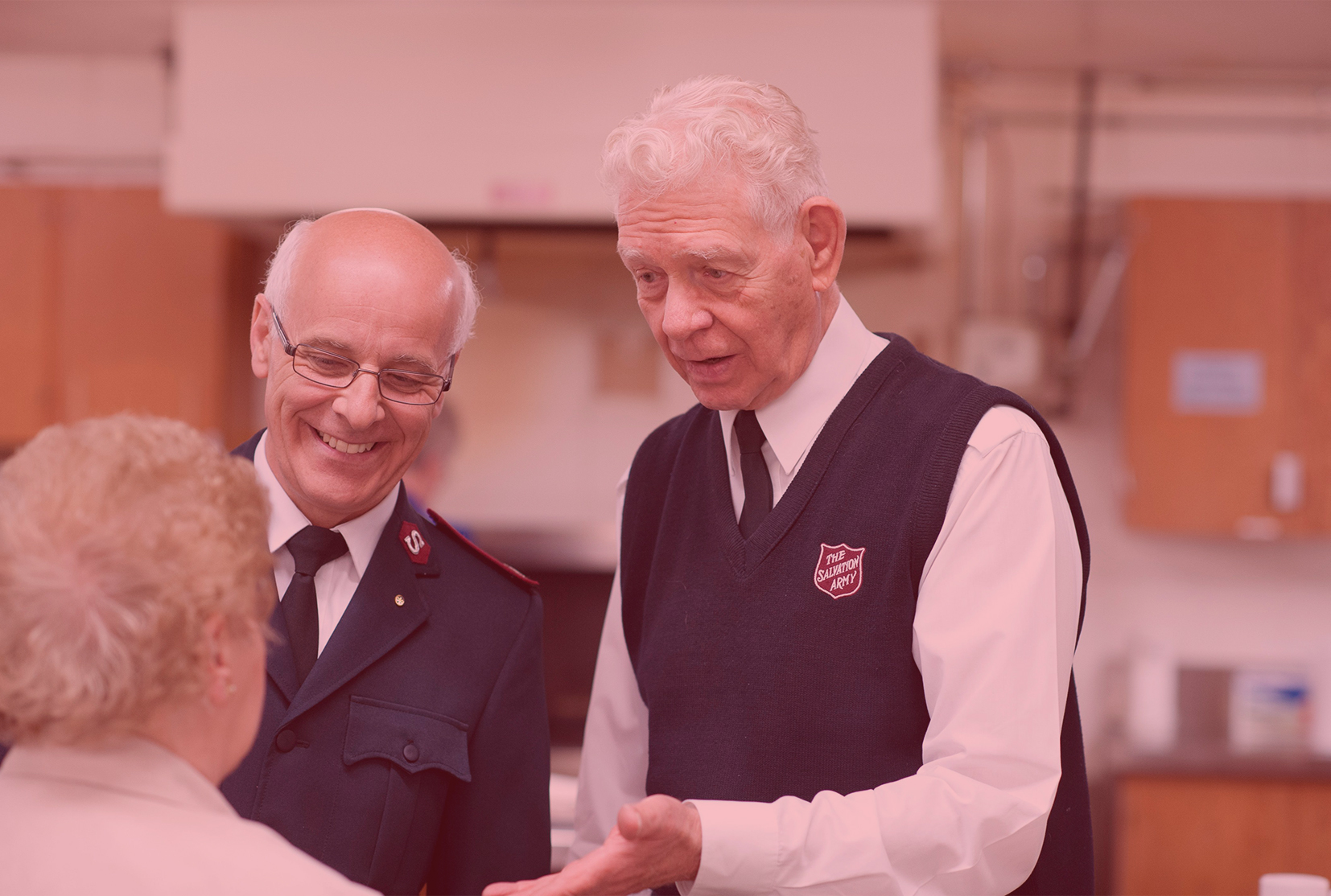 An older officer and soldier smile and talk to a senior.