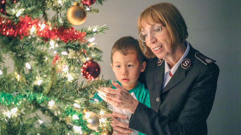 Commissioner Susan McMillan decorates a Christmas tree with a child from an Army daycare program