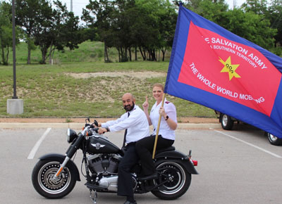 Two people riding a motorcycle while holding The Salvation Army flag