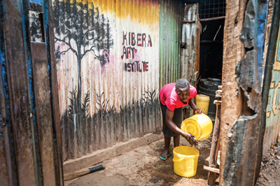 A young girl cleans a plastic water pail in front of a mural that reads, “Kibera Art Institute”