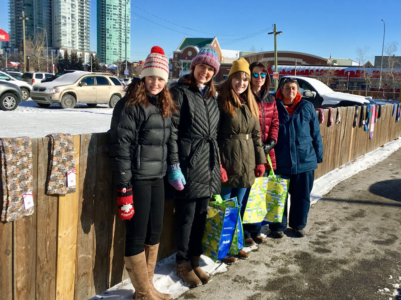 CommuKNITy Cares volunteers place hand-knit scarves on fences in Calgary