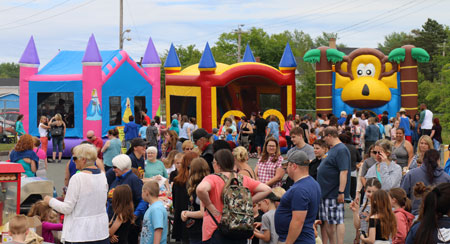 A large crowd of people gathers near bouncy castles at the block party