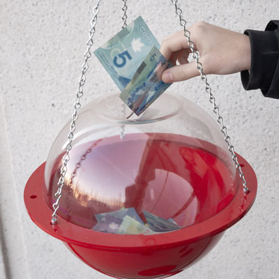 A hand puts a five-dollar bill in a Salvation Army kettle