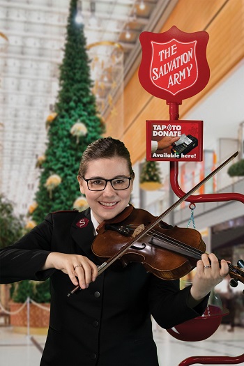 Captain Laura plays her violin near a Salvation Army Christmas kettle and a Christmas tree