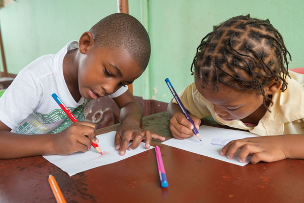 Two children sit at a table, colouring