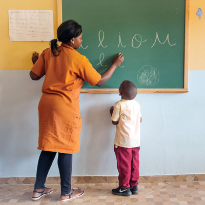 A female teacher writes on a blackboard, while a child watches and learns