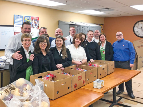 A group of Sobeys employees, with Major Corey Vincent, stand next to a table of Christmas hampers