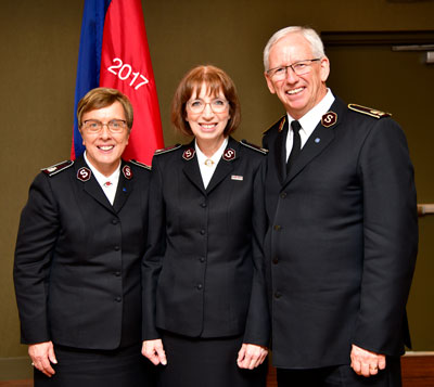 Commissioner Rosalie Peddle, Commissioner Susan McMillan and General Brian Peddle stand with the flag