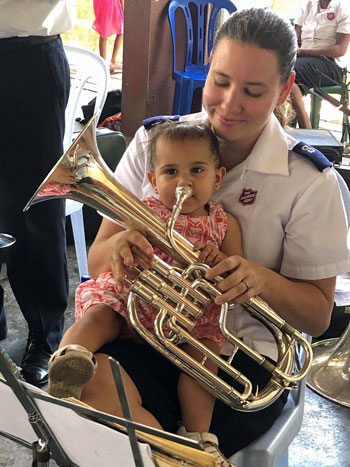 April Barthau plays a brass instrument while holding Hadassah