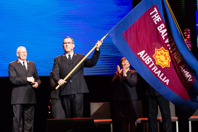 Commissioner Floyd Tidd waves the Army flag at the inauguration of the new Australia Territory as General Brian Peddle looks on