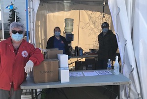 Three volunteers with masks on stand in a tent ready to serve