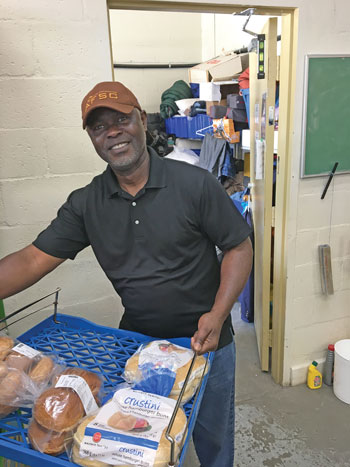 Benny Ogwuegbu holds a blue skid with buns on it to sort for the food hampers