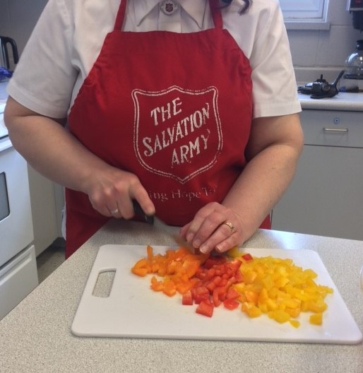 A Salvation Army corps officer wearing a red apron volunteers cuts fresh food for delivery