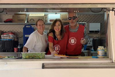 Three EDS workers stand at the window of a community response unit, ready to serve food