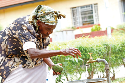 A resident at Mitanda turns on outdoor faucet to wash fruit