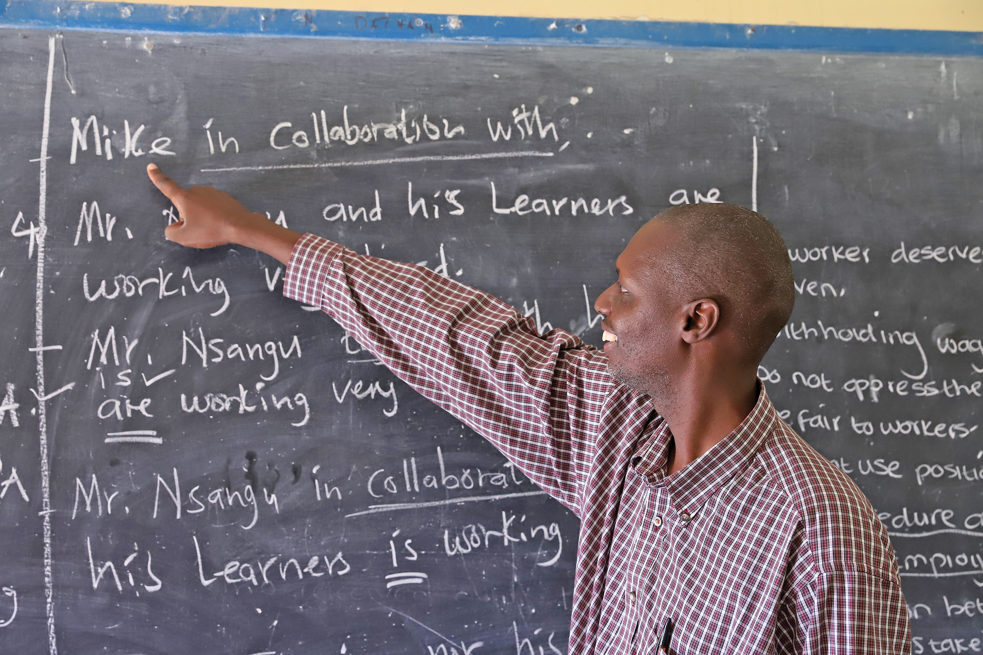 Kenneth Sinakaimbi, teacher, points to text on a chalk board