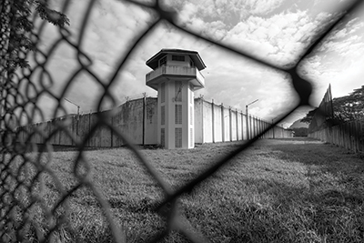 Black and white image of a prison, looking through a chain-link fence