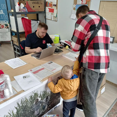 Captain Oleg, seated at a table, is offering assistance to a man and a young child