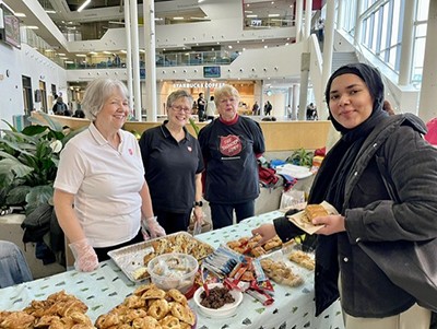 Three women behind a food table. A college student takes food from the table and is smiling.