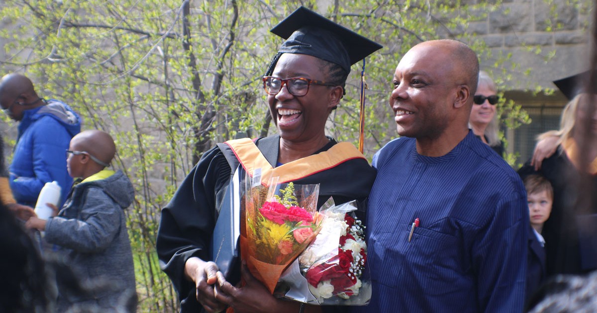 A woman wearing a graduation cap and gown shares a smile with a supporter