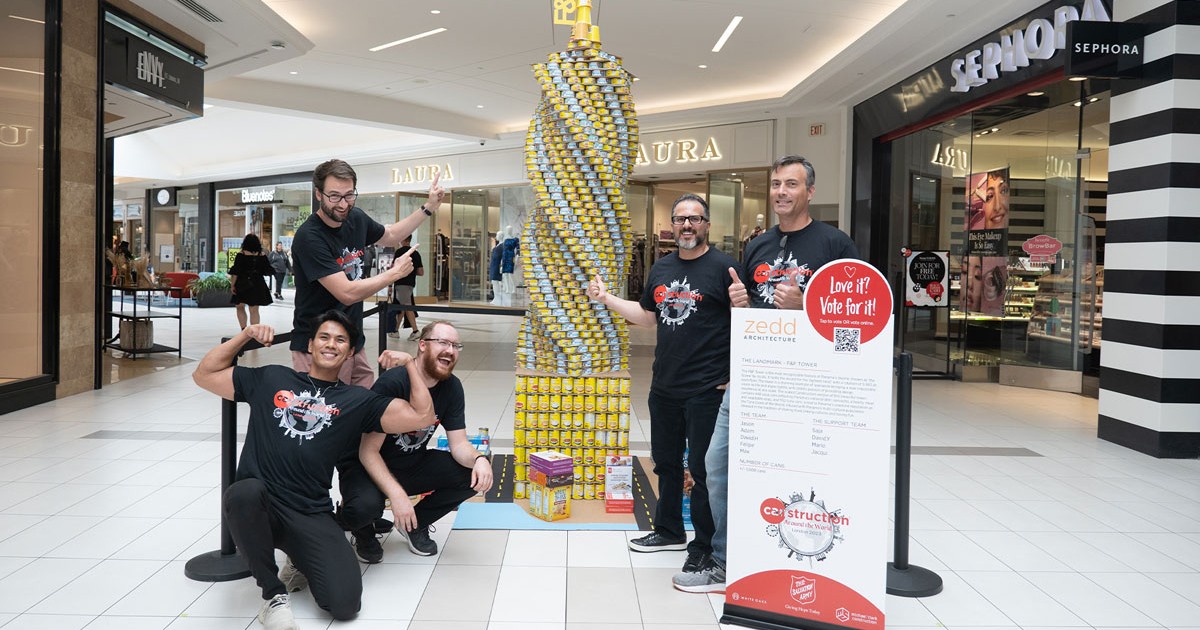 People pose with a building made out of canned goods