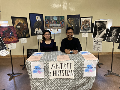 Two people sitting at a table surrounded by paintings