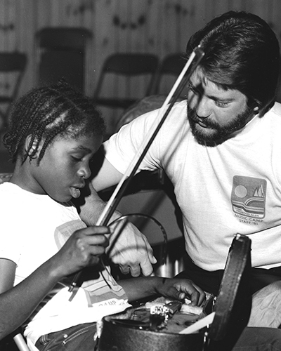 A man teaches a young woman to play violin