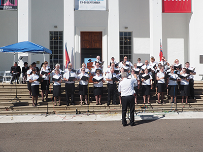 A choir performs outside a white building