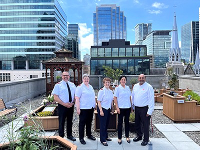 A group of people stand in a rooftop garden with high-rises in the background