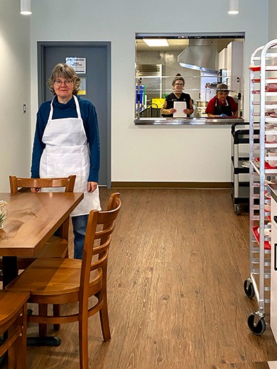 A woman in an apron standing in front of a table in Sally's Place.