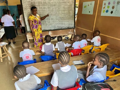 A teacher stands at the front of a classroom and teaches young children