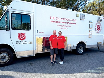 Two volunteers in red "HOPE" shirts stand in front of a Salvation Army canteen truck