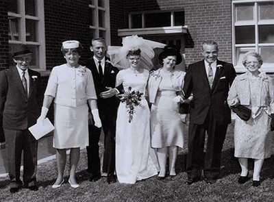 Black and white photo of Margaret Dewey as a bride with her husband, Bruce, and family, standing in front of the Fenelon Falls Corps, Ont.