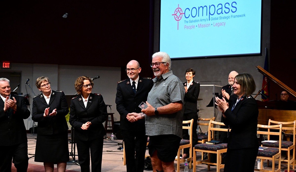 A man presents an award to another man, while others watch and clap