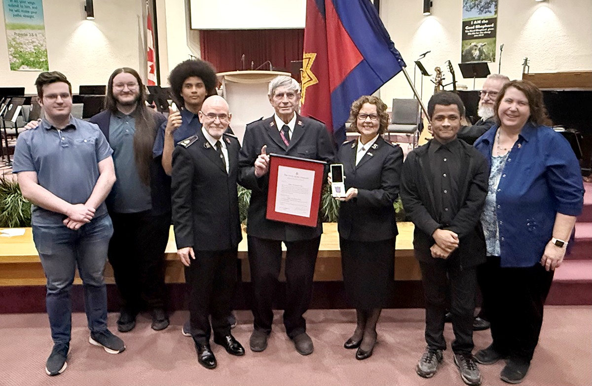 A group of nine people stand together; man in centre holds a certificate