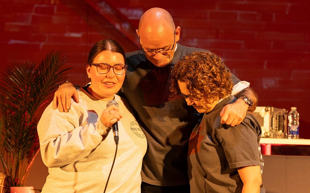 Three people pray with heads bowed