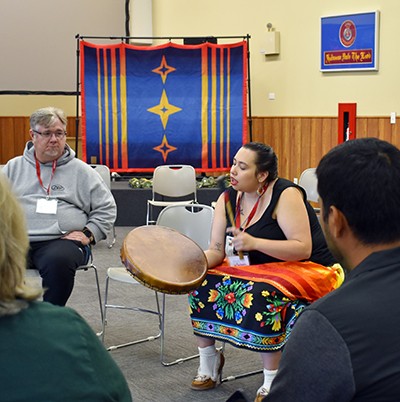 A woman sits in a circle with others and drums