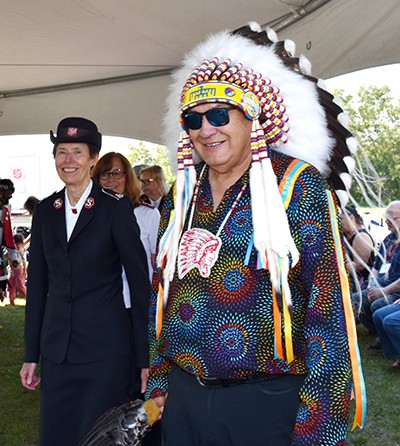 A woman wearing a Salvation Army uniform and a man wearing an Indigenous head dress walk together