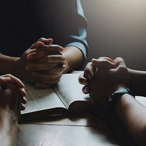 Image of three people praying in a bible study.