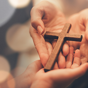 Image of a wooden cross on people's hands.