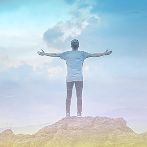 Image of a man on top of a hill, looking to the sky with opened arms